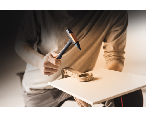 Mann benutzt Hammer und Fliesenschneider zum Bearbeiten einer Fliese