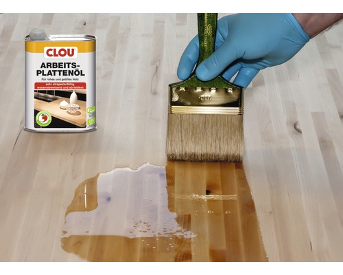 Auftragen von Arbeitsplattenöl mit Pinsel auf einer Holzoberfläche neben einer Dose Clou Arbeitsplattenöl.