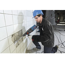 Handwerker mit Bohrhammer beim Entfernen von Fliesen von einer Wand.