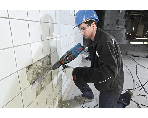 Handwerker mit Bohrhammer beim Entfernen von Fliesen von einer Wand.