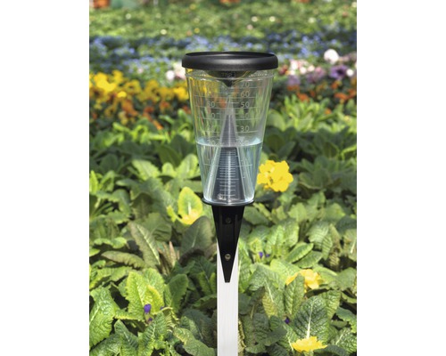 Pluviomètre dans le jardin avec des fleurs en arrière-plan