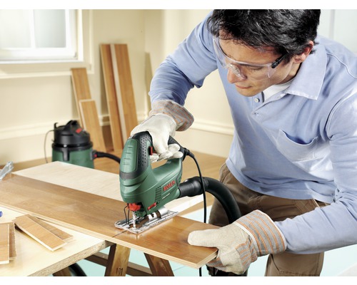 Un homme est en train de scier une planche en bois avec une scie sauteuse sur un établi.