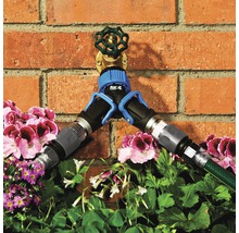 Robinet d''eau avec distributeur et tuyaux d''arrosage raccordés devant un mur de briques