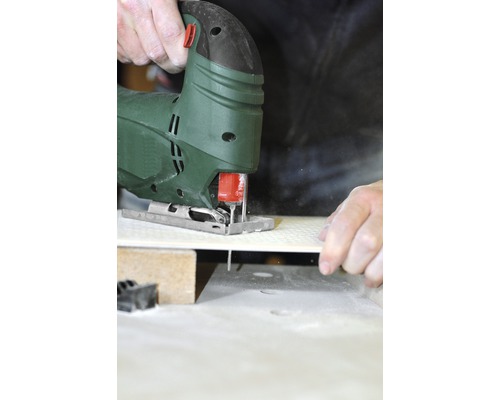 Une scie sauteuse coupe une pièce sur un établi.