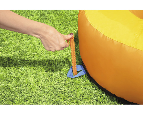 Befestigung eines orangefarbenen Luftsofas mit einem Hering im Gras