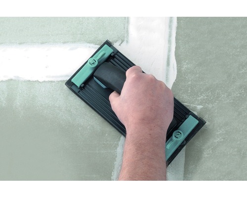 Eine Hand verwendet ein Schleifbrett zum Glätten einer gespachtelten Wand.