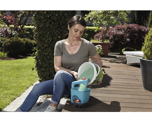 Eine Frau füllt einen Düngerstreuer in einem Garten.