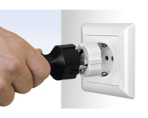 Une main insère une fiche de contact de protection dans une prise de courant avec sécurité enfant.