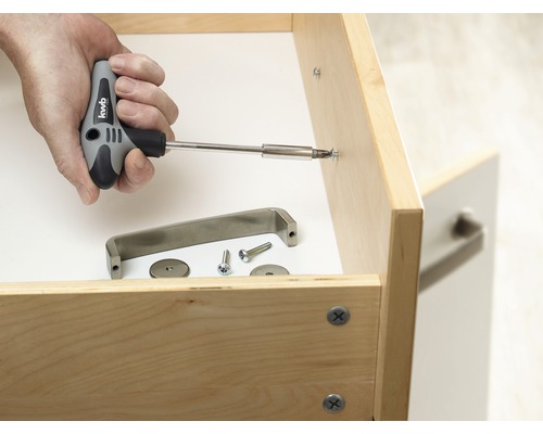 Une main visse une poignée de meuble à un tiroir avec un tournevis