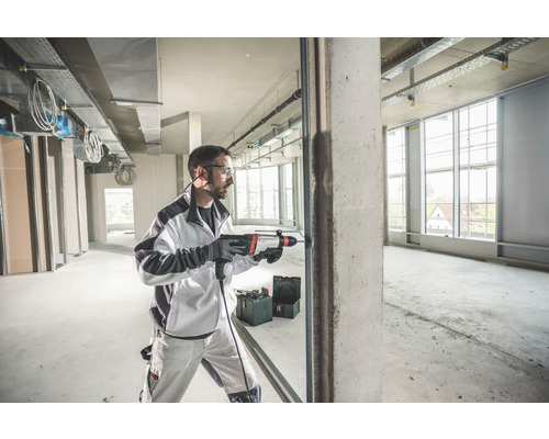 Mann bohrt mit einem Bohrhammer in einem Rohbau ein Loch in Beton.