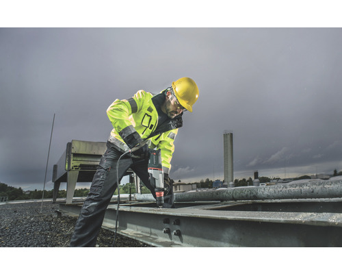 Ein Bauarbeiter bohrt mit einer Bohrmaschine in ein Metallstück.