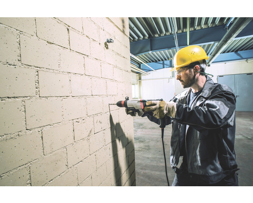 Ein Mann bohrt mit einer Schlagbohrmaschine ein Loch in eine Ziegelwand.