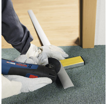 Artisan coupant une plinthe avec un outil multifonction. Niveau à bulle à portée de main.