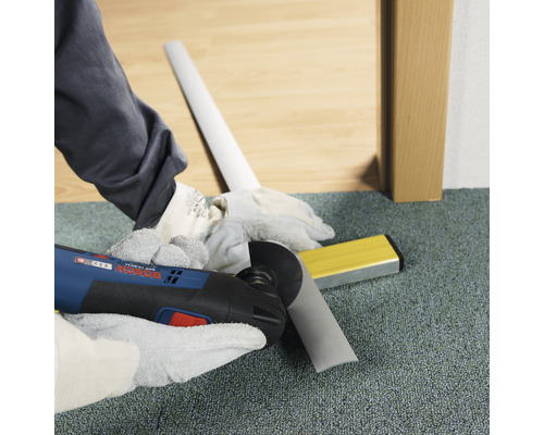 Artisan coupant une plinthe avec un outil multifonction. Niveau à bulle à portée de main.