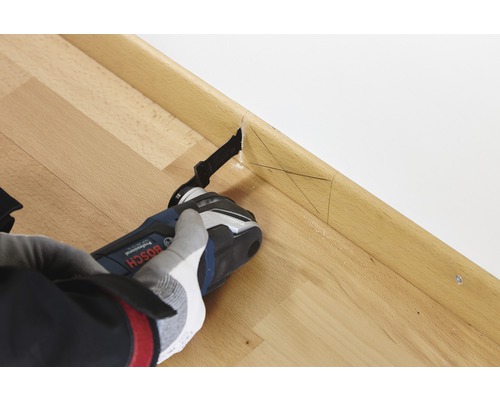 Une personne utilise une scie oscillante multifonction sur une plinthe en bois pour faire une coupe précise.