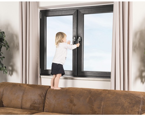 Un enfant se tient sur un canapé et essaie d''ouvrir une fenêtre.