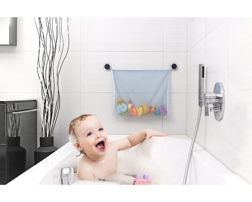 Un bébé est assis dans la baignoire avec des jouets de bain et un filet à jouets sur le mur.