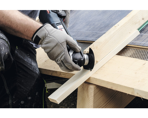 Une personne coupe une planche de bois avec un outil multifonction.