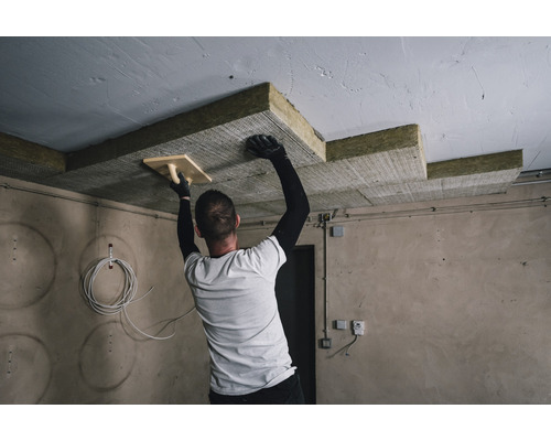 Un homme installe une isolation de plafond avec une spatule