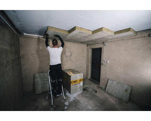 Un homme installe des panneaux isolants au plafond d''une pièce à l''aide d''une échelle.