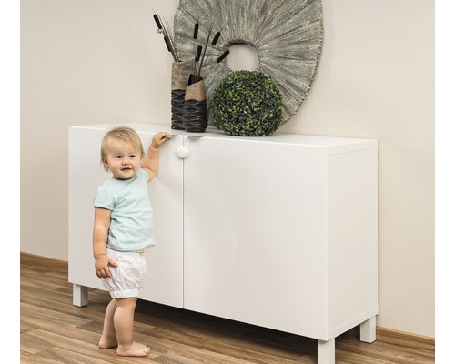 Un enfant se tient à côté d''une armoire blanche avec une sécurité enfant.