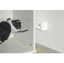 Une personne scie un trou dans une étagère en bois à côté d''une prise de courant avec un outil multifonctionnel.