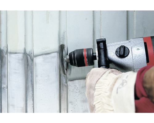 Une personne utilise une perceuse avec une brosse métallique pour nettoyer une surface métallique