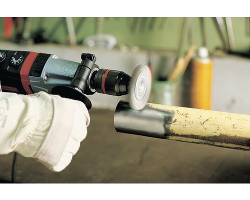 Une personne utilise une perceuse avec une brosse métallique sur un tuyau pour enlever la rouille.