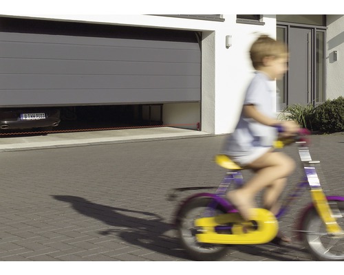 Une porte sectionnelle avec barrière lumineuse sécurise un garage pendant qu''un enfant passe à vélo.