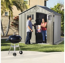 Scène de jardin avec remise à outils, barbecue et deux personnes portant du charbon de bois
