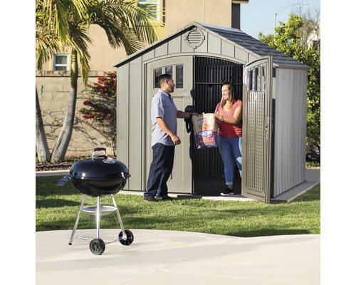 Scène de jardin avec remise à outils, barbecue et deux personnes portant du charbon de bois