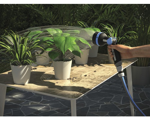 Hand bewässert Pflanzen mit einem Gartenschlauchaufsatz auf einem Tisch.