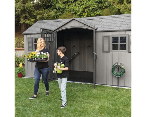Scène de jardin avec une remise, une femme et un garçon portant des articles de jardinage