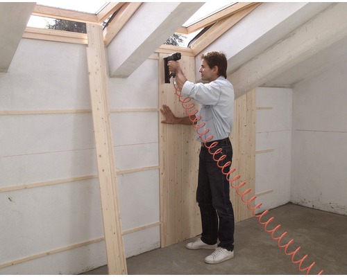 Un homme fixe des panneaux de bois avec un cloueur pneumatique sur un mur dans les combles.
