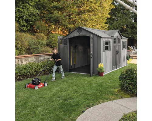 Scène de jardin avec abri de jardin et personne tondant la pelouse