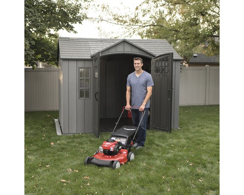 Mann mit Rasenmäher vor einem grauen Gartenhaus