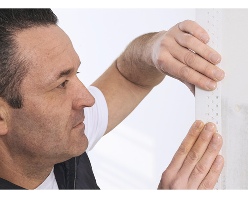 Ein Mann befestigt eine Putzprofilschiene an einer Wand.