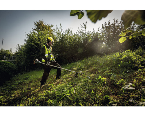Eine Person mit Sicherheitsausrüstung verwendet eine Motorsense zum Schneiden von Gras