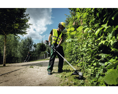 Eine Person schneidet mit einer Motorsense eine Hecke im Garten.