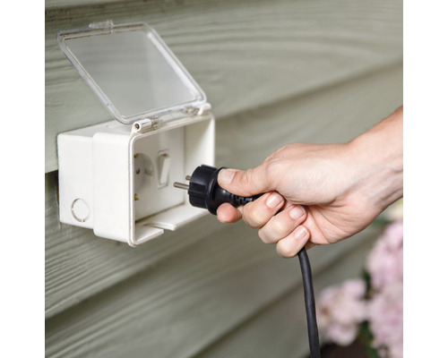 Une personne branche une prise dans une prise extérieure étanche.