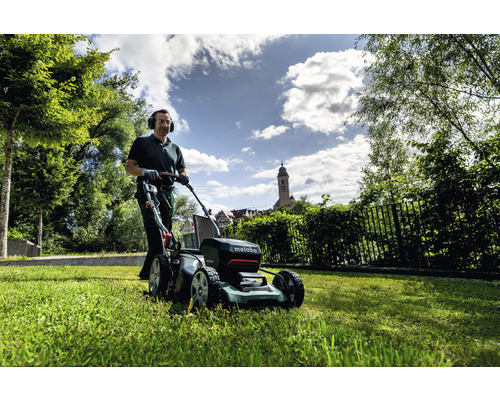 Mann mäht Rasen mit einem Metabo Akku-Rasenmäher im Garten.