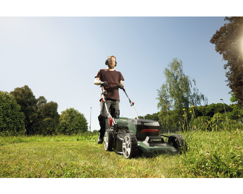 Mann mäht Rasen mit einem Metabo Rasenmäher im Garten.