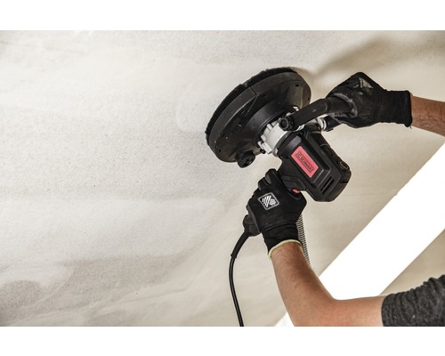 Un homme ponce un plafond avec une ponceuse à plafond.