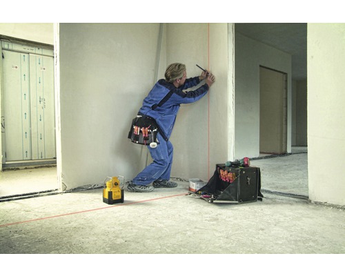 Artisan marquant un mur avec un niveau laser et un stylo dans une construction brute