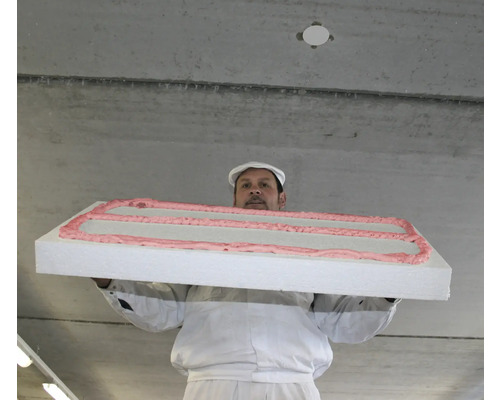 Ein Mann in Arbeitskleidung hält eine Isolierplatte mit Klebstoff an einer Betondecke.