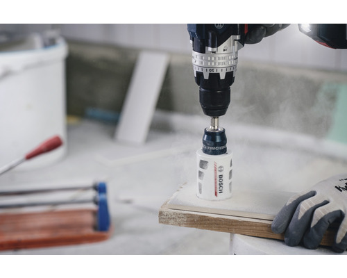 Bohrmaschine mit Lochsäge bohrt ein Loch in eine Fliese. Bosch Logo