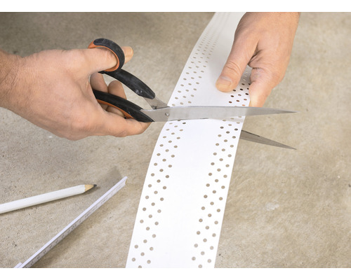 Eine Person schneidet ein gelochtes Kantenschutzprofil mit einer Schere zu.