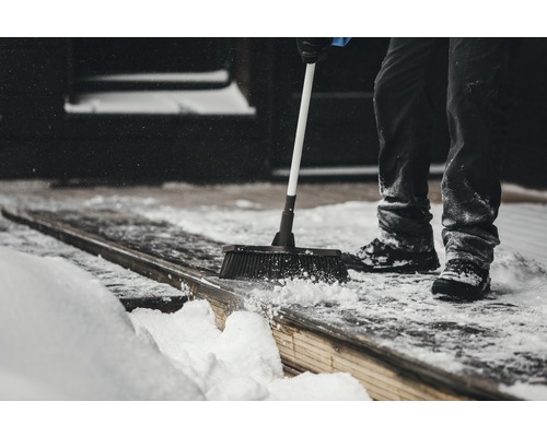 Une personne balaie la neige d''une terrasse en bois avec un balai