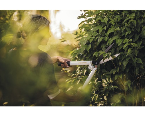 Une femme taille une haie avec un taille-haie Fiskars.