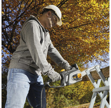 Mann mit Schutzhelm und Schutzbrille sägt Holz mit einer Kettensäge.